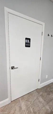 White interior door with contemporary hardware, light gray walls, white baseboards, and large format floor tile
