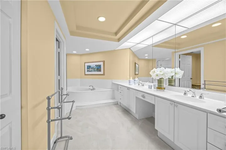 Full bath with light colored carpet, a bath, double vanity, recessed lighting, and a tray ceiling