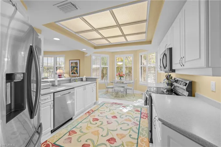 Kitchen featuring stainless steel appliances, white cabinets, a raised ceiling, plenty of natural light, and light countertops