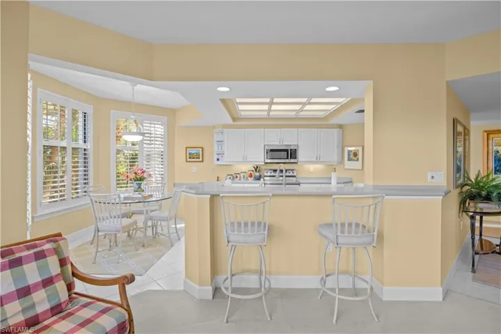 Kitchen with white cabinets, a kitchen breakfast bar, a peninsula, light stone countertops, and stainless steel appliances