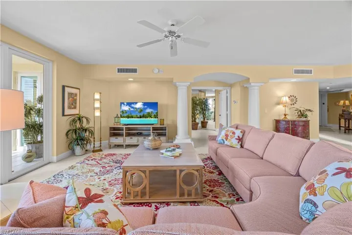 Living room with ornate columns, arched walkways, a ceiling fan, and healthy amount of natural light