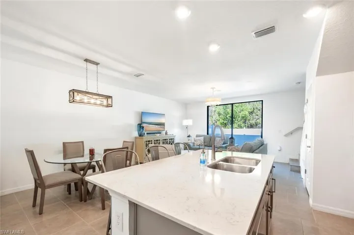 Kitchen featuring open floor plan, a kitchen island with sink, pendant lighting, light stone countertops, and a kitchen breakfast bar