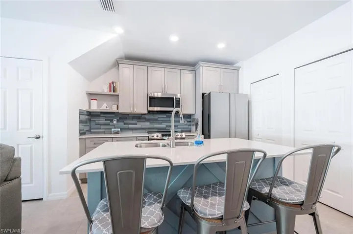 Kitchen with decorative backsplash, light countertops, an island with sink, fridge, and gray cabinetry