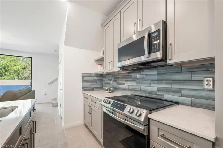Kitchen featuring appliances with stainless steel finishes, gray cabinets, backsplash, open floor plan, and light stone counters