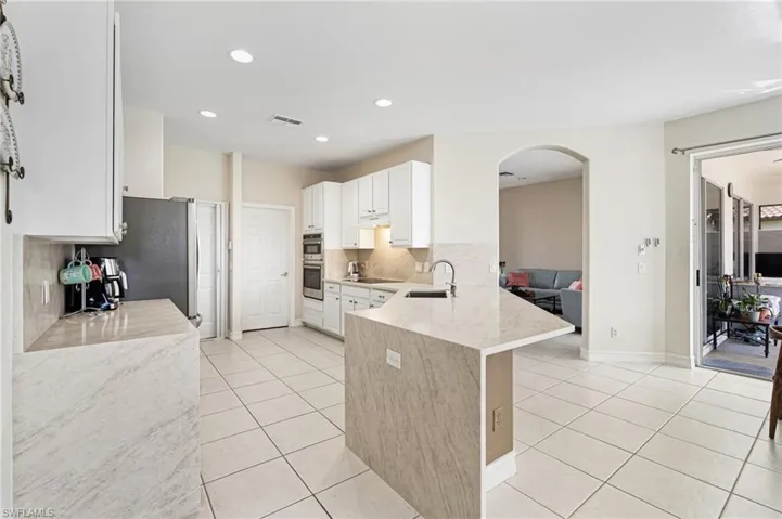 Kitchen with light stone countertops, decorative backsplash, arched walkways, a peninsula, and light tile patterned flooring