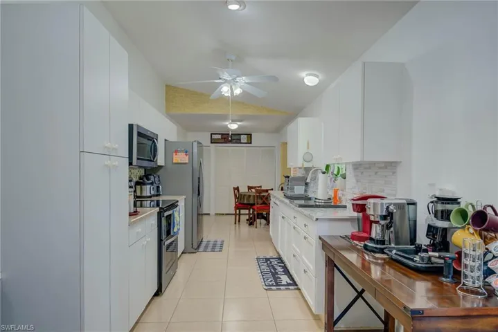 Kitchen featuring light tile patterned floors, tasteful backsplash, appliances with stainless steel finishes, vaulted ceiling, and white cabinets