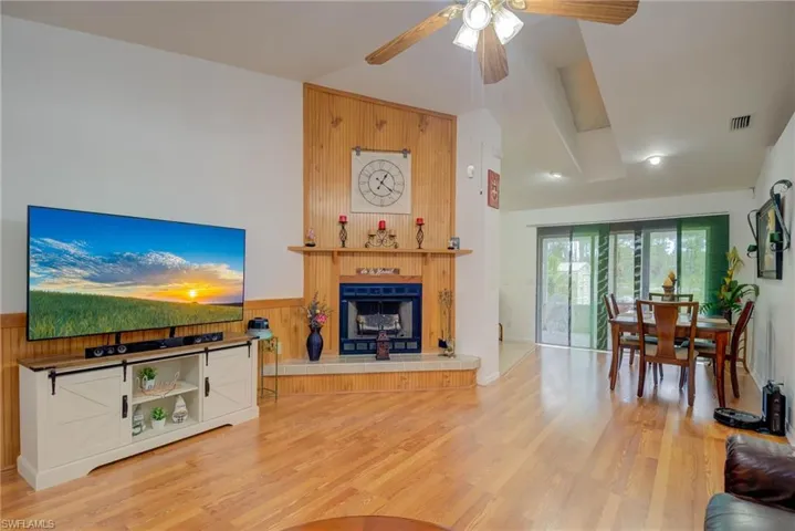 Living room featuring wood walls, light wood-style flooring, a tile fireplace, a ceiling fan, and a wainscoted wall