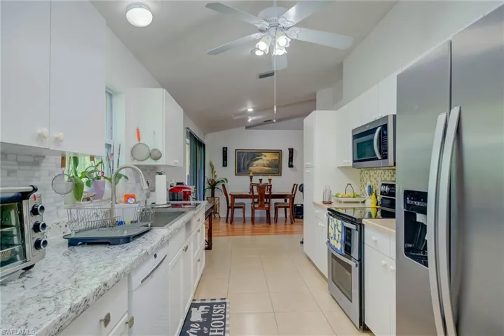 Kitchen with tasteful backsplash, stainless steel appliances, light tile patterned flooring, vaulted ceiling, and white cabinetry