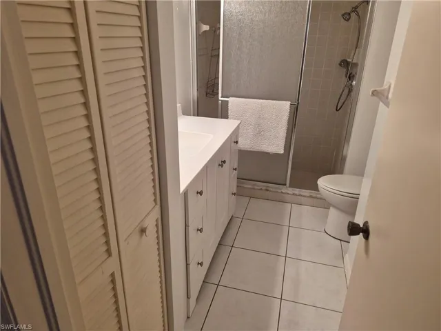 Bathroom featuring a white vanity with integrated sink, white tile flooring, a glass-enclosed shower with tiled walls, and louvered bi-fold closet doors