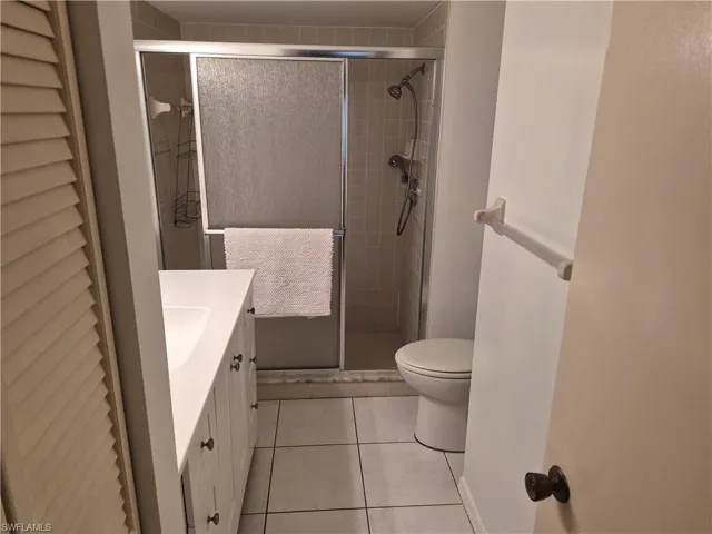 Bathroom featuring a shower with sliding glass doors, white vanity with integrated sink, white base cabinetry with dark hardware, and a tile floor