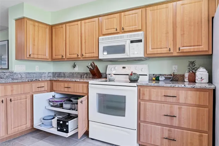 Kitchen with light stone countertops, tile patterned flooring, and white appliances