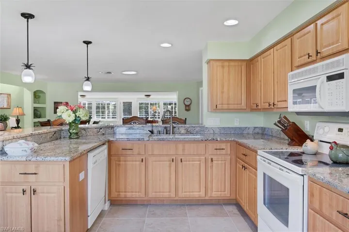 Kitchen with sink, decorative light fixtures, white appliances, and light brown cabinets