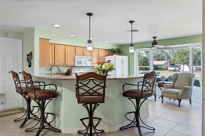 Kitchen with a breakfast bar, white appliances, decorative light fixtures, light tile patterned flooring, and light stone counters