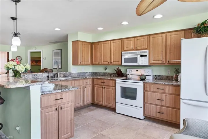 Kitchen featuring sink, light stone counters, pendant lighting, white appliances, and light tile patterned floors