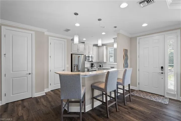 Kitchen featuring a kitchen breakfast bar, light stone counters, appliances with stainless steel finishes, decorative light fixtures, and dark hardwood / wood-style flooring