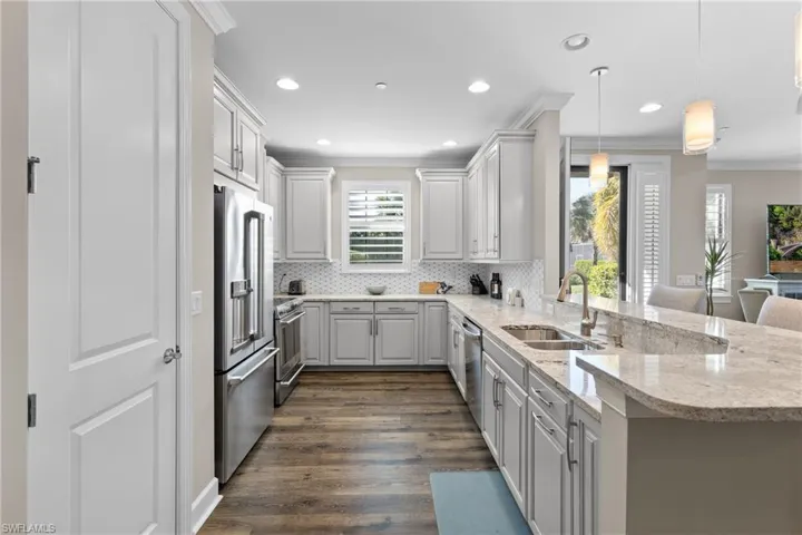 Kitchen with stainless steel appliances, sink, decorative light fixtures, dark hardwood / wood-style floors, and white cabinetry