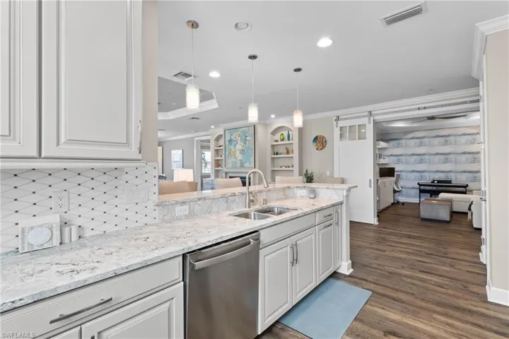 Kitchen with kitchen peninsula, stainless steel dishwasher, sink, pendant lighting, and white cabinetry