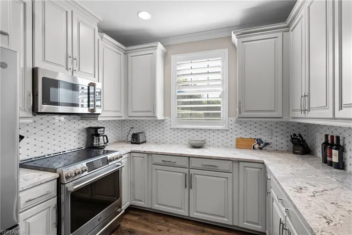 Kitchen with white cabinets, dark hardwood / wood-style flooring, appliances with stainless steel finishes, and tasteful backsplash