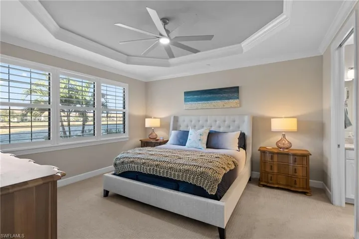 Carpeted bedroom featuring a raised ceiling, ceiling fan, and crown molding