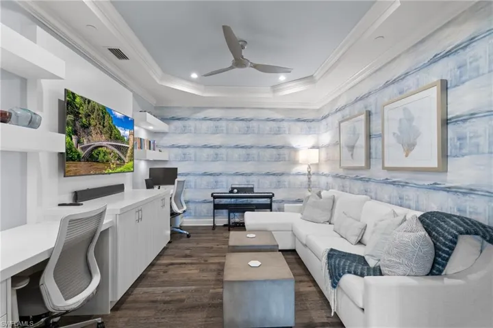 Living room with a raised ceiling, crown molding, ceiling fan, built in desk, and dark hardwood / wood-style flooring