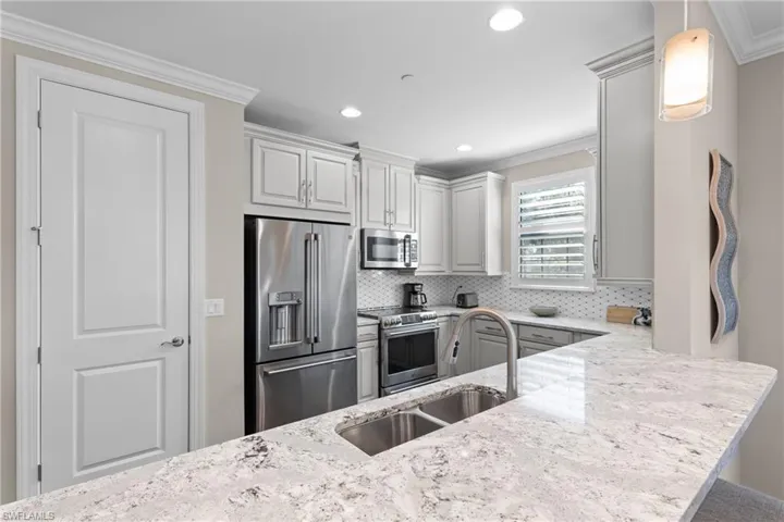 Kitchen with sink, crown molding, hanging light fixtures, kitchen peninsula, and stainless steel appliances