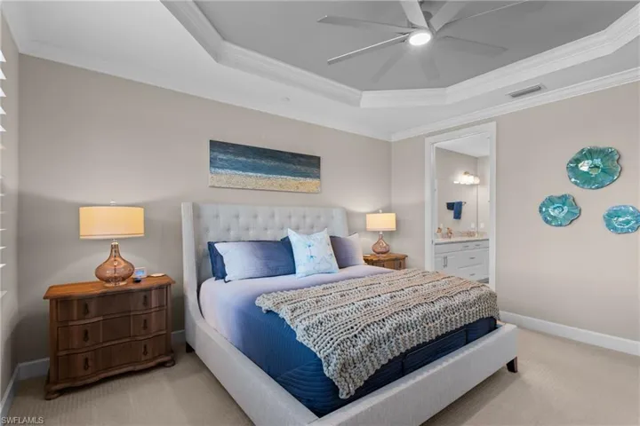 Bedroom with ensuite bathroom, a raised ceiling, ceiling fan, ornamental molding, and light colored carpet
