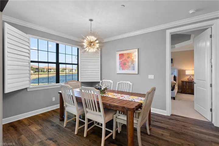 Dining space with a water view, ornamental molding, dark wood-type flooring, and a chandelier