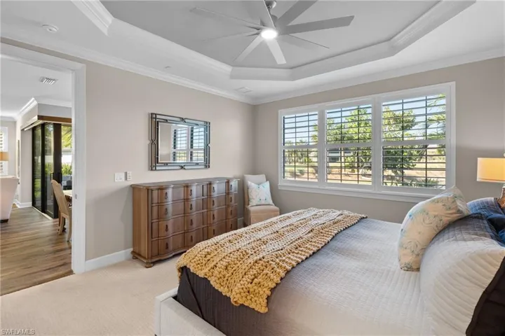 Bedroom with ceiling fan, crown molding, light carpet, and a tray ceiling