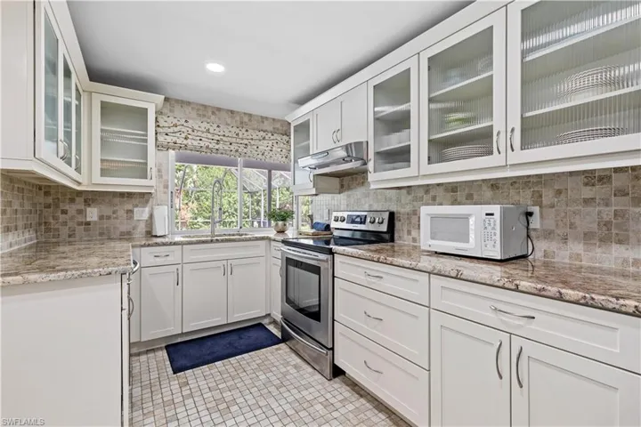 Kitchen featuring sink, decorative backsplash, light tile patterned floors, stainless steel electric range oven, and white cabinets