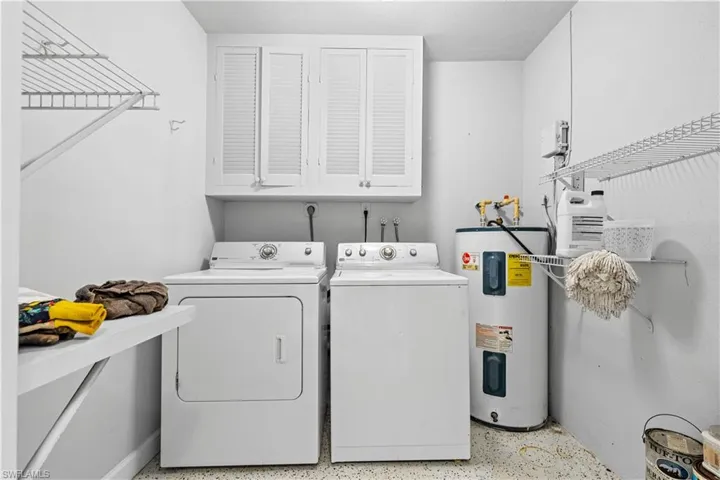 Washroom featuring washer and clothes dryer, water heater, and cabinets