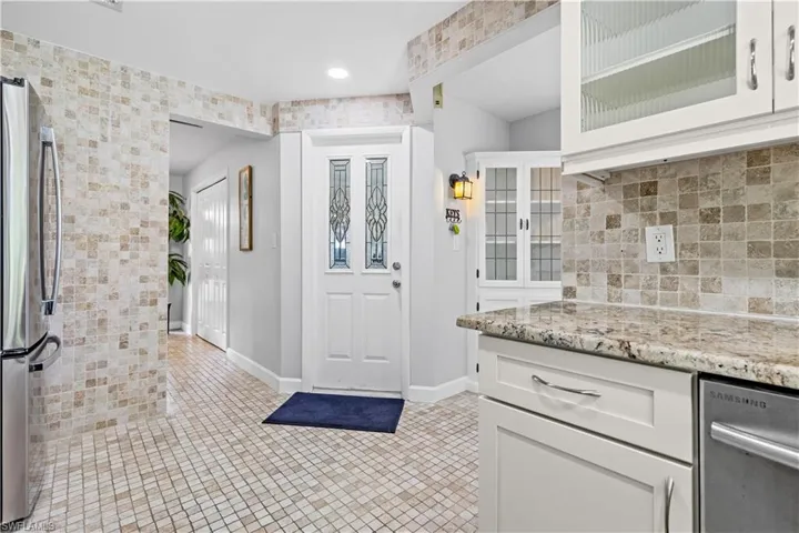 Kitchen with decorative backsplash, white cabinetry, light stone counters, light tile patterned floors, and stainless steel fridge