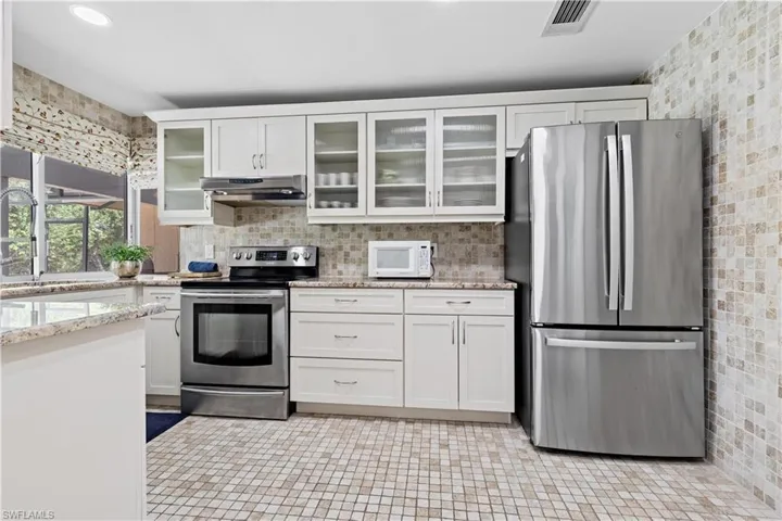 Kitchen with tasteful backsplash, white cabinetry, light stone counters, light tile patterned flooring, and stainless steel appliances