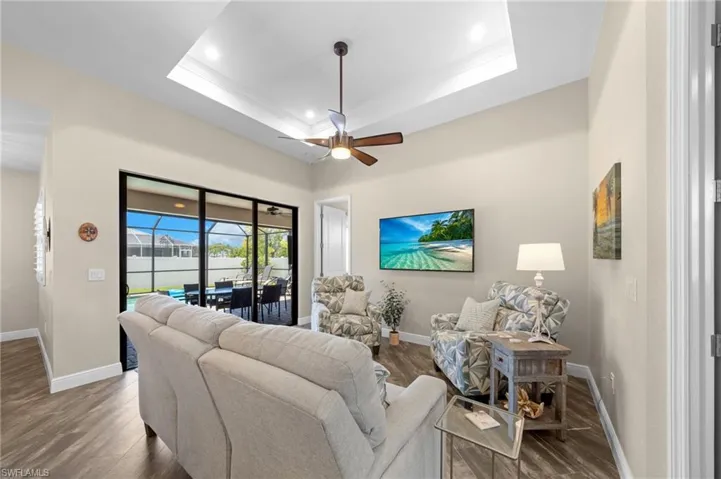Living area with a tray ceiling, a ceiling fan, wood finished floors, and recessed lighting