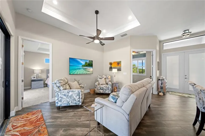 Living area featuring a raised ceiling, french doors, ornamental molding, dark wood-type flooring, and recessed lighting