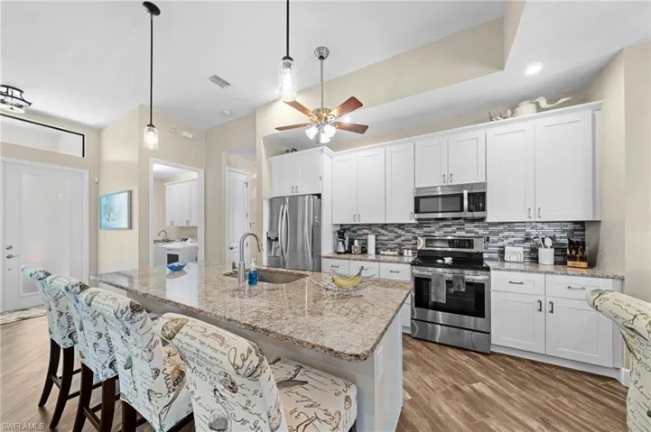 Kitchen featuring a kitchen bar, stainless steel appliances, white cabinets, and tasteful backsplash