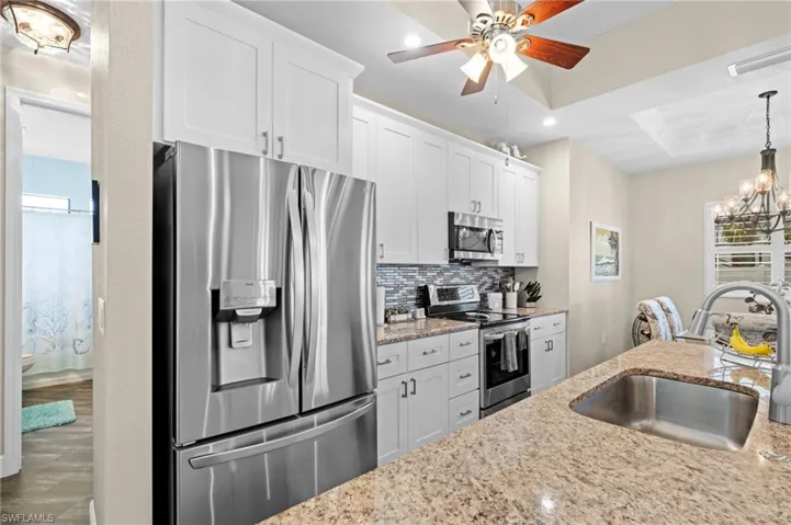 Kitchen featuring stainless steel appliances, decorative backsplash, a chandelier, hanging light fixtures, and white cabinets