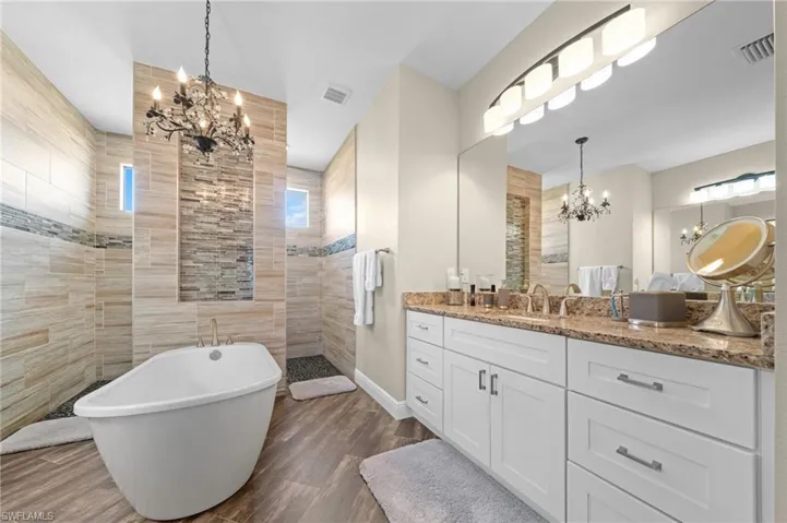 Bathroom featuring a chandelier, a walk in shower, a soaking tub, vanity, and dark wood-style flooring