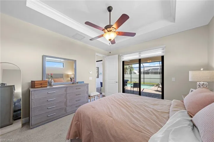 Bedroom with a tray ceiling, light colored carpet, a ceiling fan, access to exterior, and crown molding