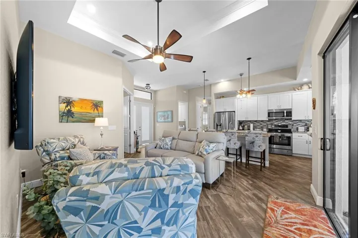 Living area with a tray ceiling, dark wood-style floors, recessed lighting, a ceiling fan, and ornamental molding
