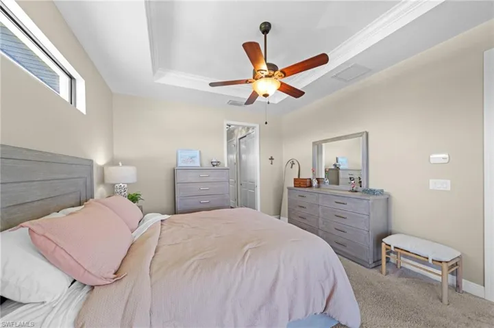 Carpeted bedroom featuring a raised ceiling, ceiling fan, and ornamental molding