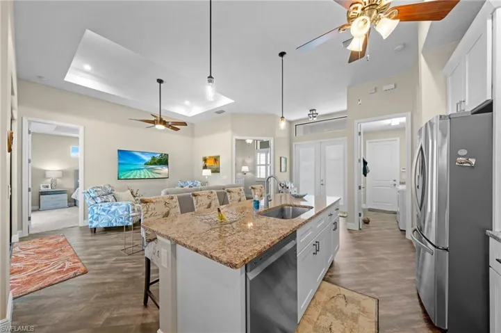 Kitchen featuring ceiling fan, a tray ceiling, a kitchen breakfast bar, appliances with stainless steel finishes, and light stone counters