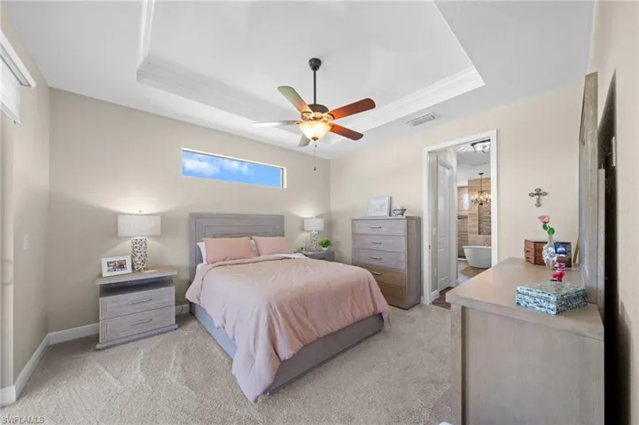 Bedroom with a tray ceiling, light carpet, ceiling fan, and ensuite bathroom
