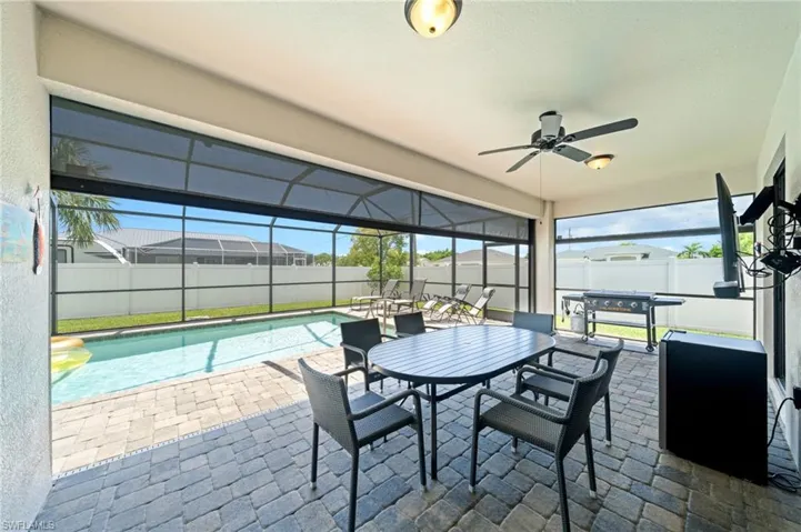 Fenced backyard with glass enclosure, a sunroom, outdoor dining area, a patio area, and a ceiling fan