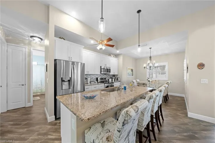 Kitchen with a breakfast bar area, light stone countertops, decorative backsplash, white cabinetry, and stainless steel appliances
