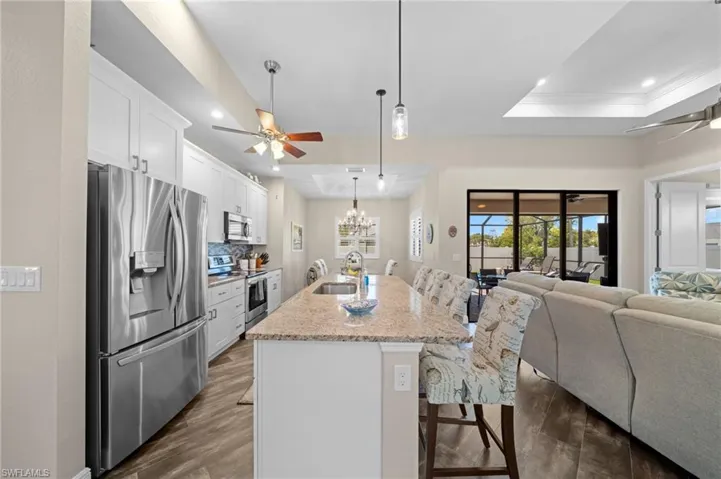 Kitchen with ceiling fan, a breakfast bar, stainless steel appliances, white cabinetry, and dark wood finished floors