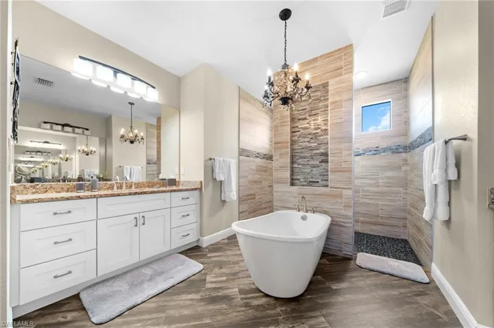 Bathroom featuring a chandelier, vanity, a soaking tub, a walk in shower, and dark wood finished floors