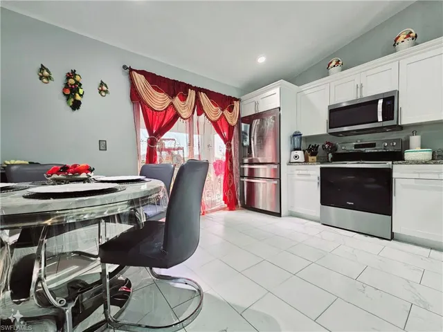 Kitchen with white cabinetry, appliances with stainless steel finishes, lofted ceiling, and light stone counters