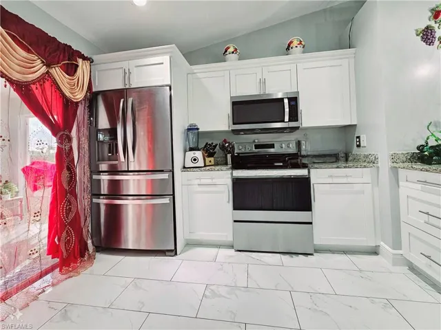 Kitchen with white cabinetry, lofted ceiling, light stone counters, and stainless steel appliances