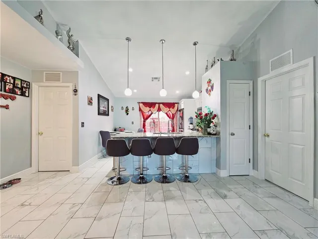 Kitchen with white cabinetry, a breakfast bar, light stone counters, kitchen peninsula, and pendant lighting