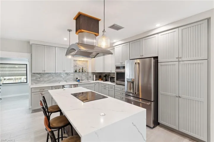 Kitchen featuring backsplash, sink, decorative light fixtures, light stone counters, and stainless steel appliances